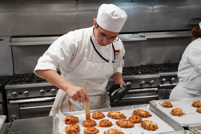 Culinary student brushing pastry with butter.