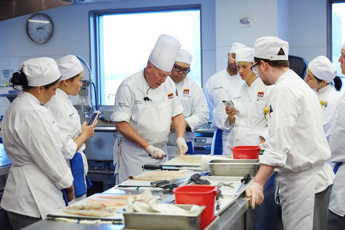 Head chef teaching students how to filet a fish.